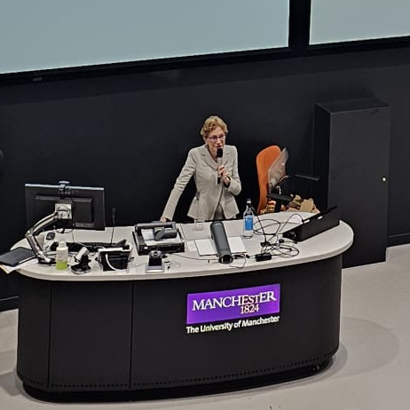 Image of Professor Dame Carol Black presenting this years TYAI lecture at a podium in a lecture theatre.