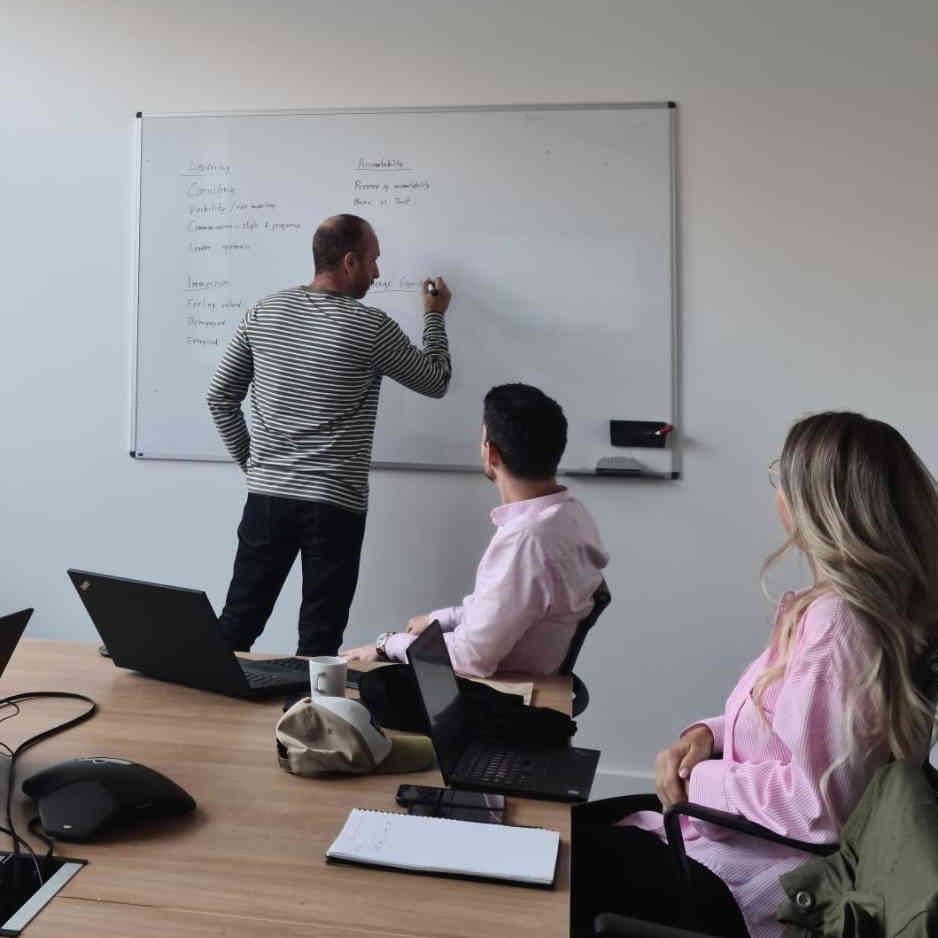 Image of a person writing on a white board, with people looking on