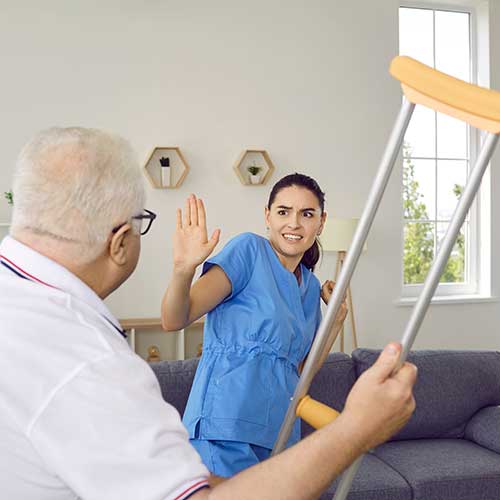 elderly man waving a crutch at a nurse.