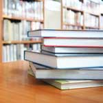 A pile of books on a table surrounded by shelves of books
